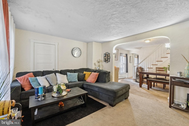 living area featuring carpet flooring, arched walkways, a textured ceiling, and stairs