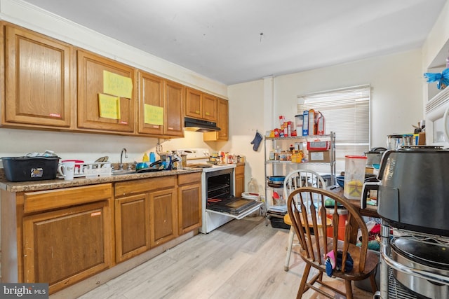 kitchen featuring brown cabinetry, white electric stove, a sink, light wood-style floors, and under cabinet range hood