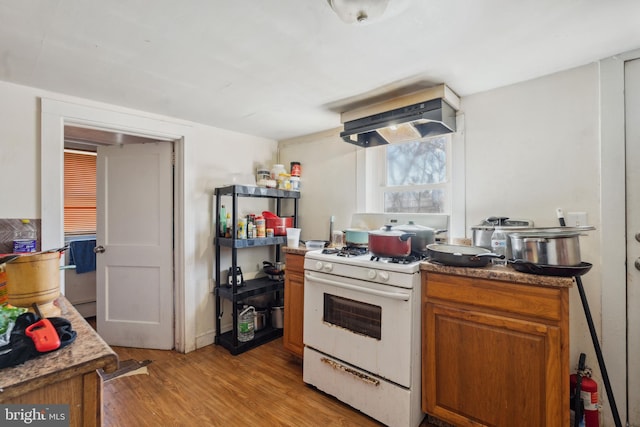 kitchen with ventilation hood, light wood-type flooring, gas range gas stove, and brown cabinetry