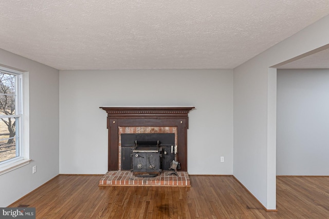 unfurnished living room with a wood stove, a textured ceiling, baseboards, and wood finished floors