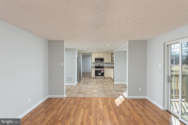 unfurnished living room with light wood-style floors, visible vents, baseboards, and a textured ceiling