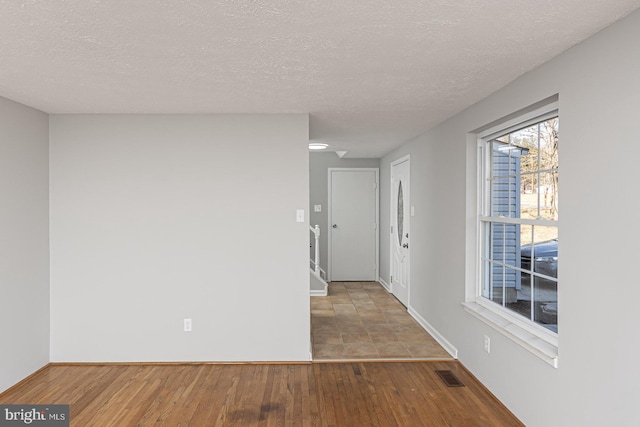 entryway with baseboards, a textured ceiling, visible vents, and wood finished floors