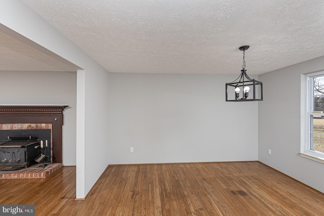 unfurnished dining area featuring a textured ceiling, wood finished floors, a wood stove, and an inviting chandelier