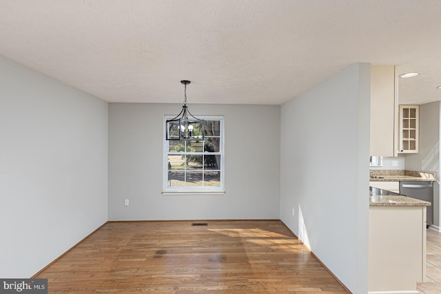 unfurnished dining area featuring visible vents, light wood-style flooring, a textured ceiling, and an inviting chandelier