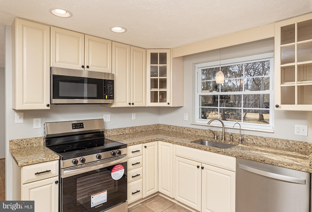 kitchen featuring light stone counters, stainless steel appliances, recessed lighting, glass insert cabinets, and a sink