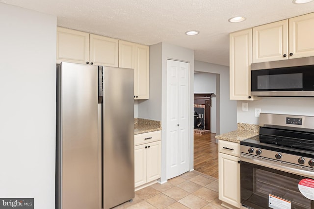 kitchen featuring a textured ceiling, stainless steel appliances, light stone counters, and cream cabinets