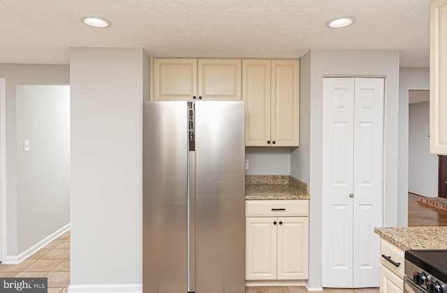 kitchen featuring light tile patterned floors, light stone counters, cream cabinets, recessed lighting, and freestanding refrigerator