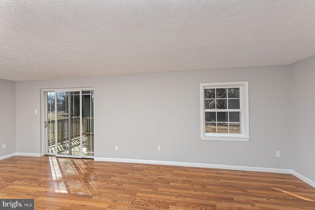 unfurnished room featuring plenty of natural light, a textured ceiling, baseboards, and wood finished floors