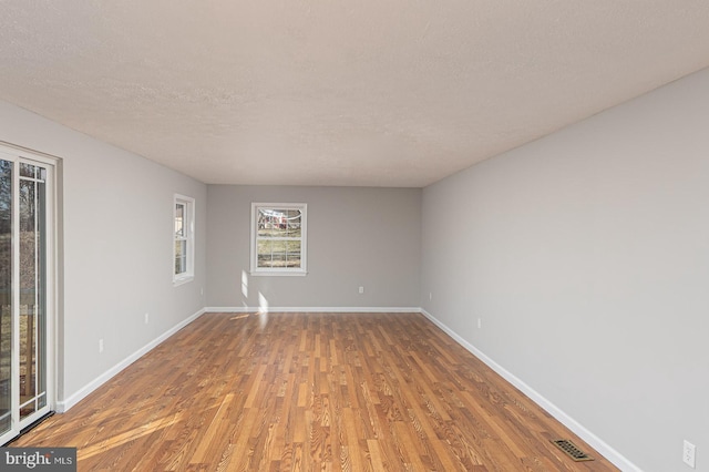 empty room featuring visible vents, a textured ceiling, baseboards, and wood finished floors