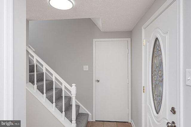 tiled entryway featuring a textured ceiling, stairs, and baseboards