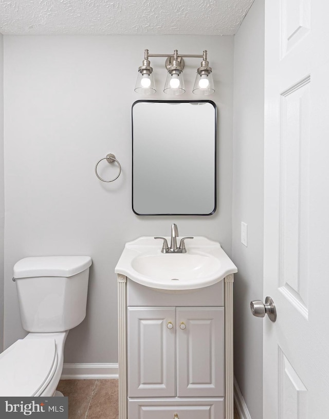 bathroom with toilet, vanity, a textured ceiling, tile patterned flooring, and baseboards