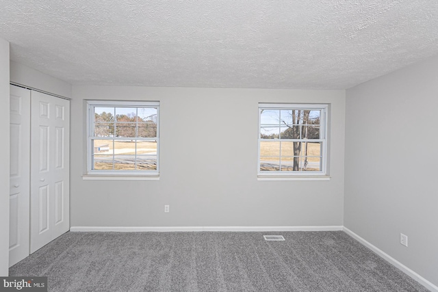 unfurnished bedroom featuring carpet, a closet, visible vents, a textured ceiling, and baseboards