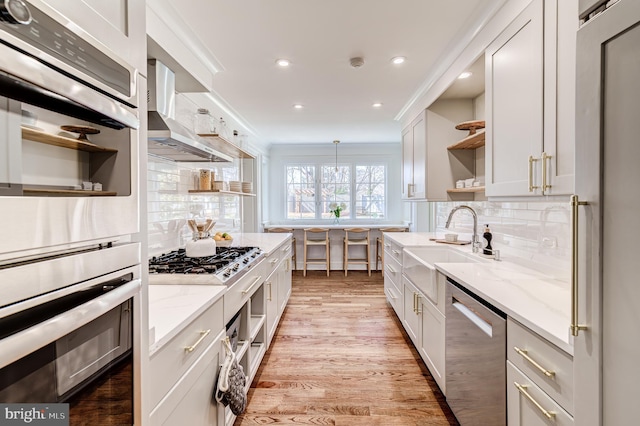 kitchen featuring wall chimney exhaust hood, light stone countertops, stainless steel appliances, crown molding, and open shelves