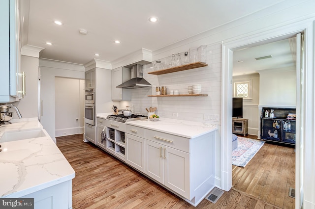 kitchen featuring ornamental molding, light wood-type flooring, a sink, and wall chimney range hood