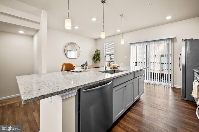 kitchen with light stone counters, dark wood-style floors, a center island with sink, appliances with stainless steel finishes, and a sink