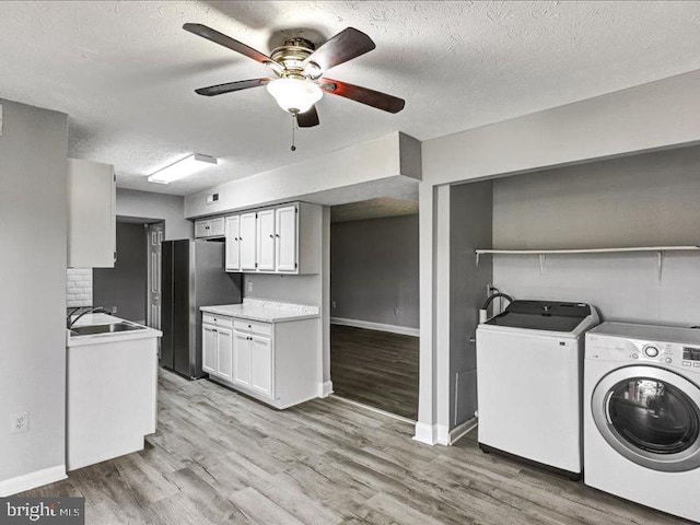 kitchen featuring washing machine and dryer, white cabinetry, light countertops, freestanding refrigerator, and light wood finished floors