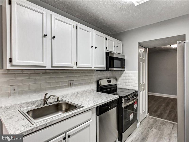 kitchen featuring a sink, stainless steel appliances, light wood-type flooring, white cabinetry, and backsplash