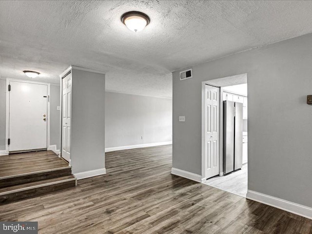 unfurnished room with visible vents, a textured ceiling, baseboards, and wood finished floors