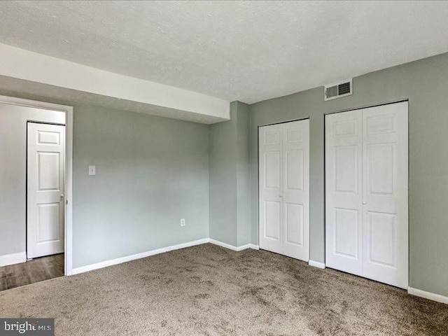 unfurnished bedroom with baseboards, visible vents, carpet, a textured ceiling, and multiple closets