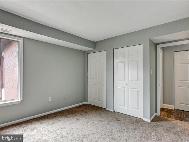 unfurnished bedroom with carpet floors, two closets, visible vents, and baseboards