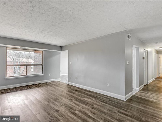 empty room with a textured ceiling, wood finished floors, visible vents, and baseboards