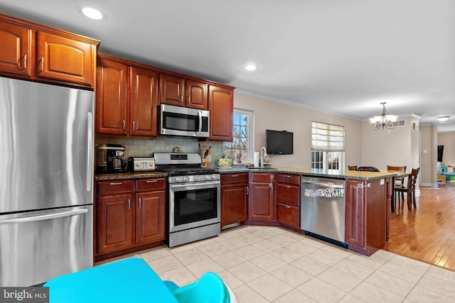 kitchen featuring a peninsula, ornamental molding, appliances with stainless steel finishes, decorative backsplash, and dark stone countertops