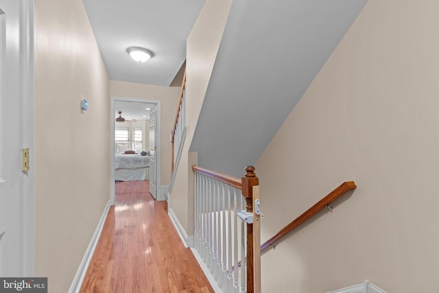 corridor with wood finished floors, an upstairs landing, and baseboards