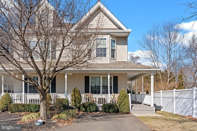 view of front of property with covered porch, roof with shingles, and fence