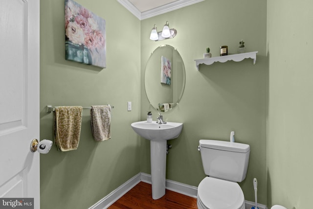 half bathroom featuring baseboards, toilet, ornamental molding, wood finished floors, and a sink