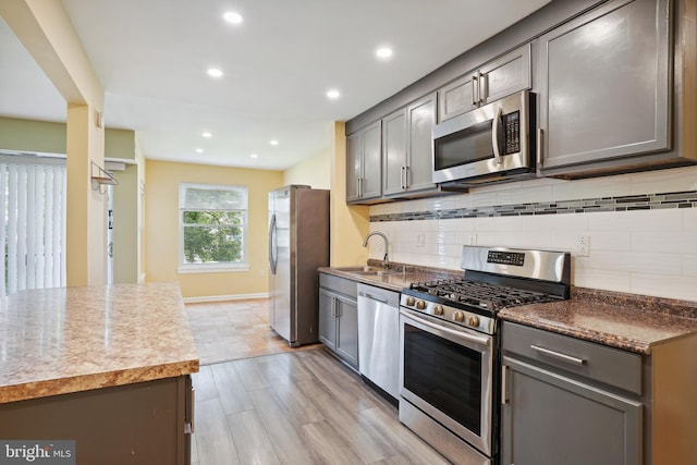 kitchen with a sink, stainless steel appliances, decorative backsplash, and gray cabinetry