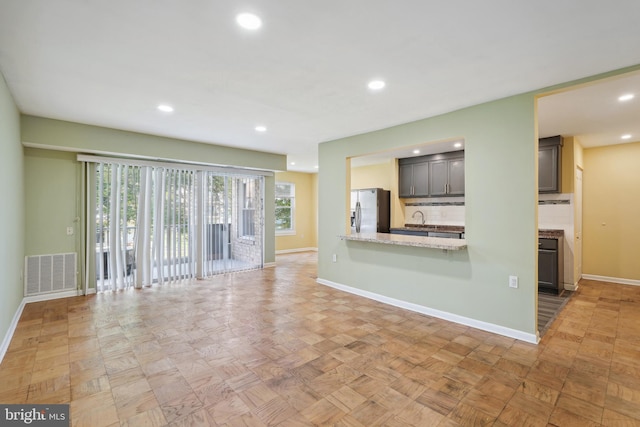 unfurnished living room with recessed lighting, visible vents, a sink, and baseboards