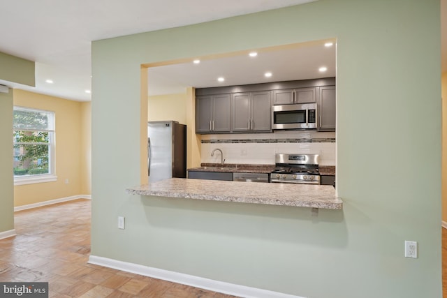 kitchen with stainless steel appliances, decorative backsplash, a sink, a peninsula, and baseboards