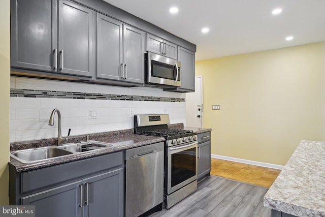 kitchen with baseboards, decorative backsplash, appliances with stainless steel finishes, light wood-type flooring, and a sink