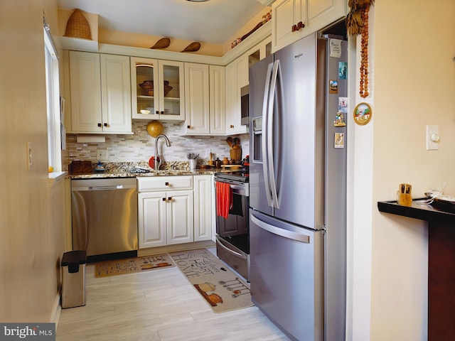 kitchen featuring tasteful backsplash, glass insert cabinets, appliances with stainless steel finishes, dark stone countertops, and a sink