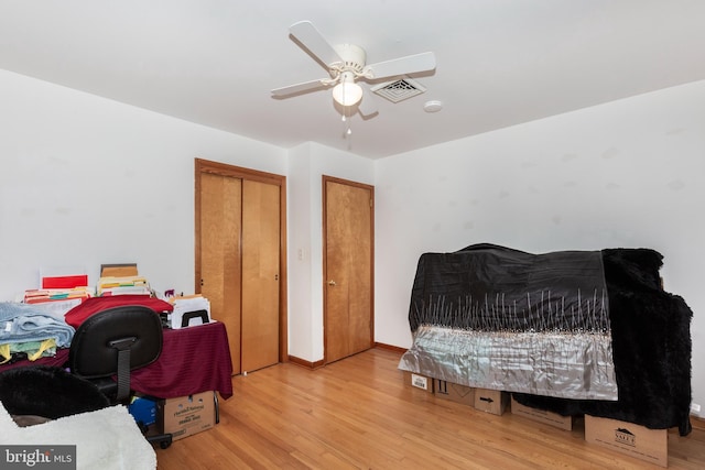 bedroom featuring ceiling fan, visible vents, baseboards, and wood finished floors