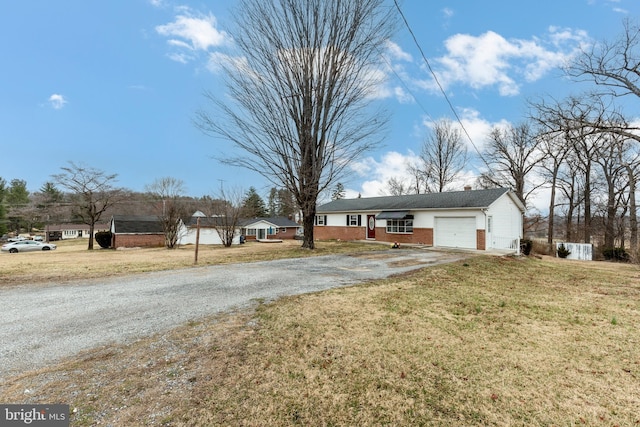 single story home with brick siding, a front yard, gravel driveway, and an attached garage