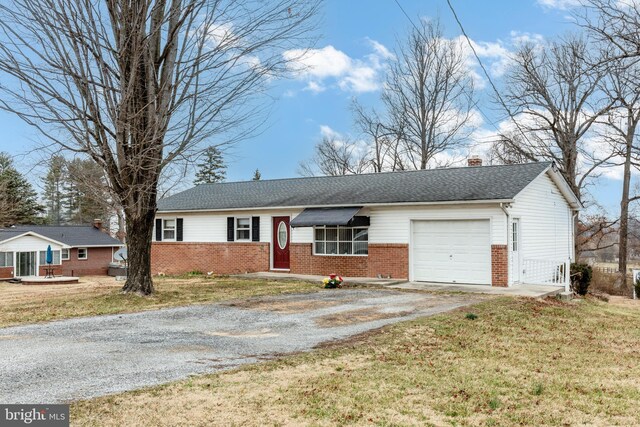 single story home featuring a garage, brick siding, gravel driveway, and a front lawn