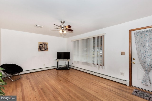 interior space featuring hardwood / wood-style flooring, a ceiling fan, visible vents, and a baseboard radiator