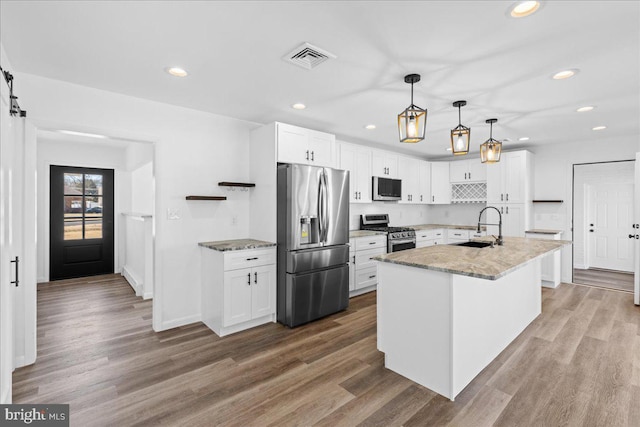 kitchen featuring visible vents, a barn door, appliances with stainless steel finishes, white cabinetry, and a sink