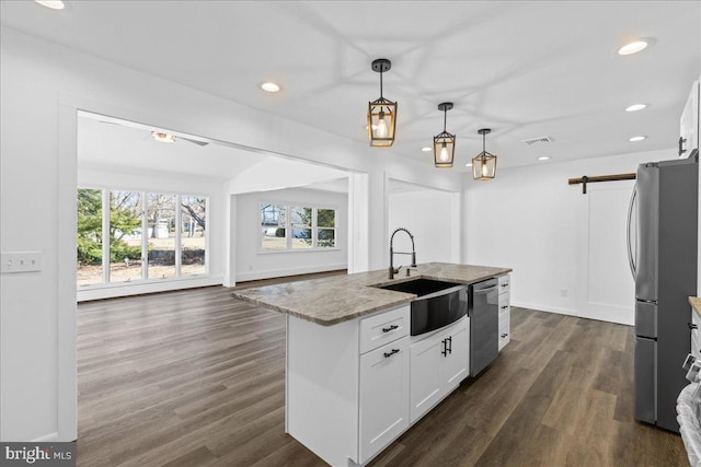 kitchen with light stone counters, stainless steel appliances, visible vents, a barn door, and a sink