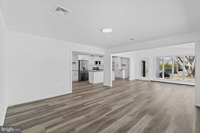 unfurnished living room with baseboards, visible vents, and wood finished floors