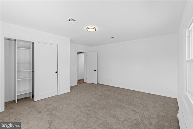 unfurnished bedroom featuring carpet floors, baseboard heating, a closet, and visible vents