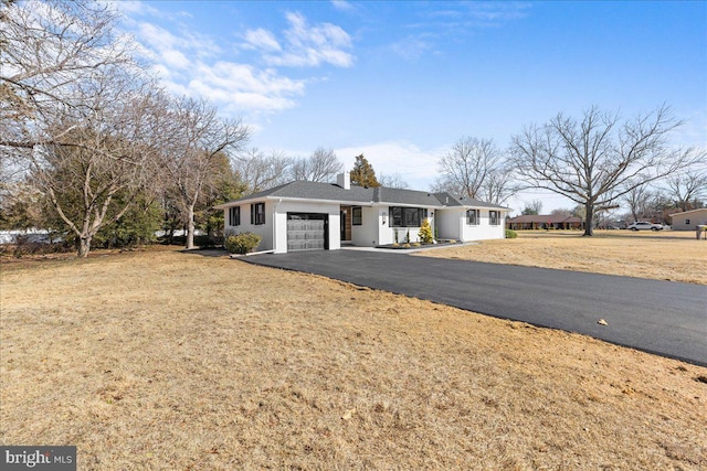 ranch-style house featuring a chimney, aphalt driveway, a front lawn, and an attached garage