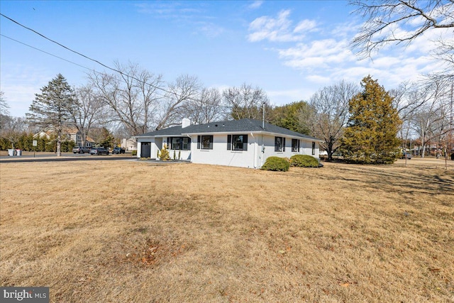 rear view of house featuring a chimney, a lawn, and an attached garage