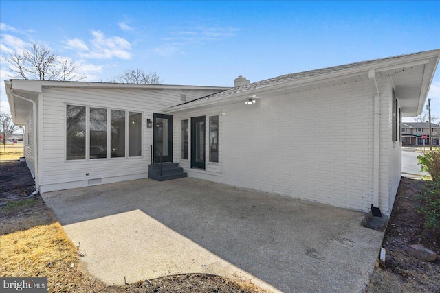 rear view of house with crawl space, brick siding, a patio, and a chimney