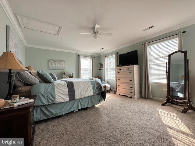 carpeted bedroom with a ceiling fan, attic access, visible vents, and crown molding