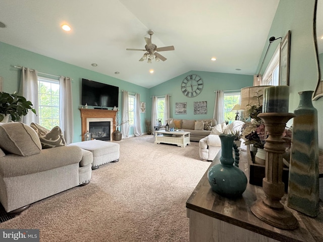 living room with a wealth of natural light, vaulted ceiling, carpet flooring, and a glass covered fireplace