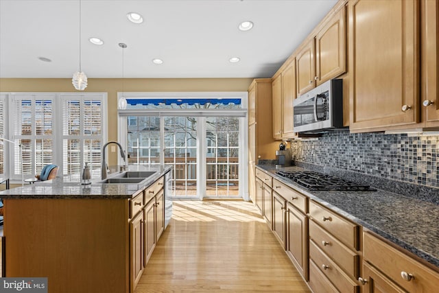 kitchen with stainless steel microwave, backsplash, light wood-type flooring, gas cooktop, and a sink