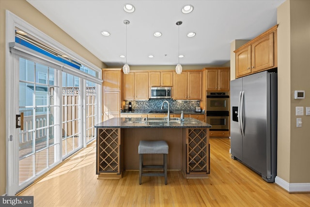 kitchen with tasteful backsplash, light wood-type flooring, an island with sink, stainless steel appliances, and a sink