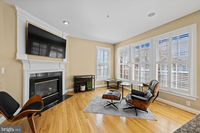 sitting room featuring a fireplace with flush hearth, wood finished floors, visible vents, and baseboards